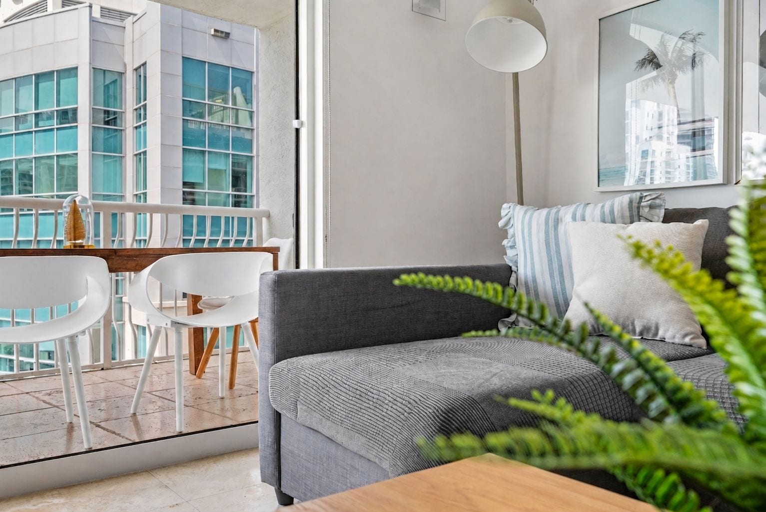 A modern living room with a grey sofa, white chairs, a wooden table, and a large window overlooking a cityscape.