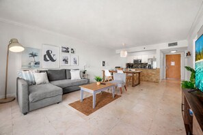 En moderne stue med en grå sofa, et sofabord og et spiseområde med stole samt et køkken i baggrunden.