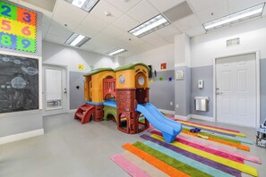 Un espace de jeux pour enfants avec un toboggan, des structures d’escalade et un tapis coloré à rayures.