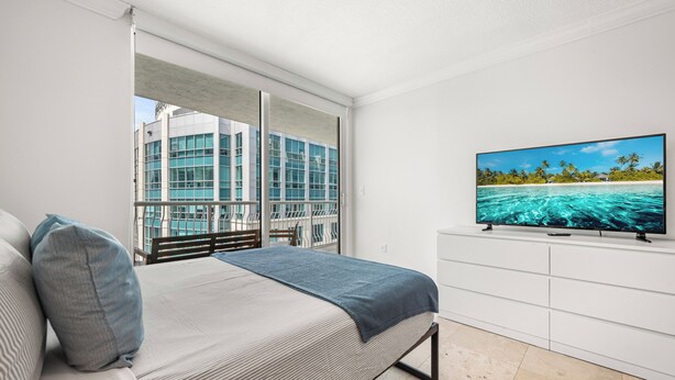 Ein Schlafzimmer mit einem Bett, einem Fernseher und Blick auf ein Gebäude und Wasser.