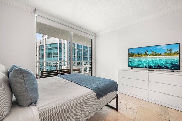Un dormitorio con cama, televisor y vista a un edificio y al agua.