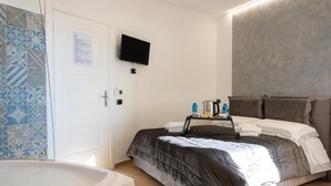 A bedroom with a bed, a TV mounted on the wall, a bedside table with toiletries, and a bathroom with a bathtub. - NA Beautiful View Rooftop-B&B - Double Room with Sea View (Napoli)