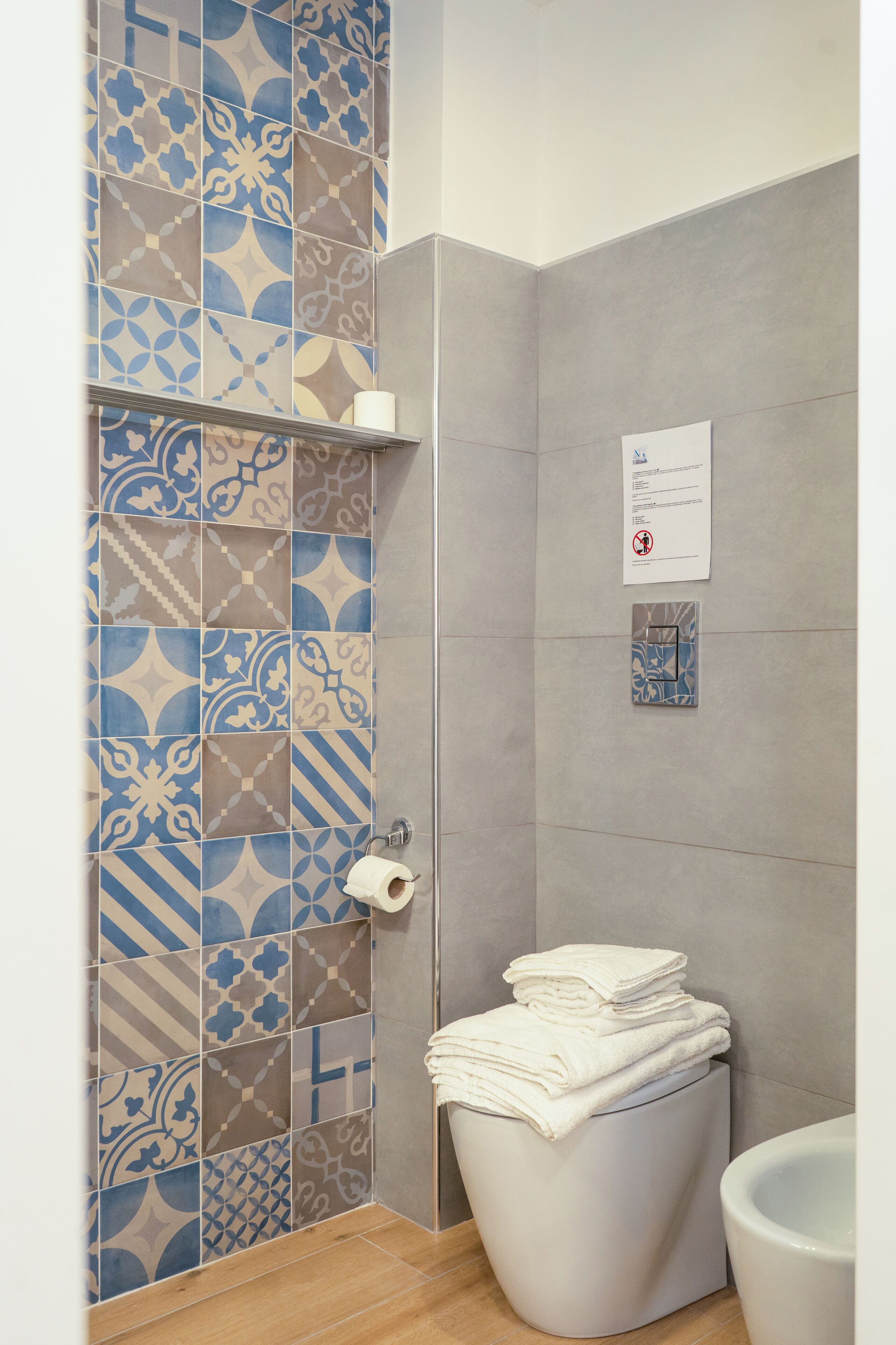Un baño con baldosas estampadas, un inodoro y una pila de toallas blancas.