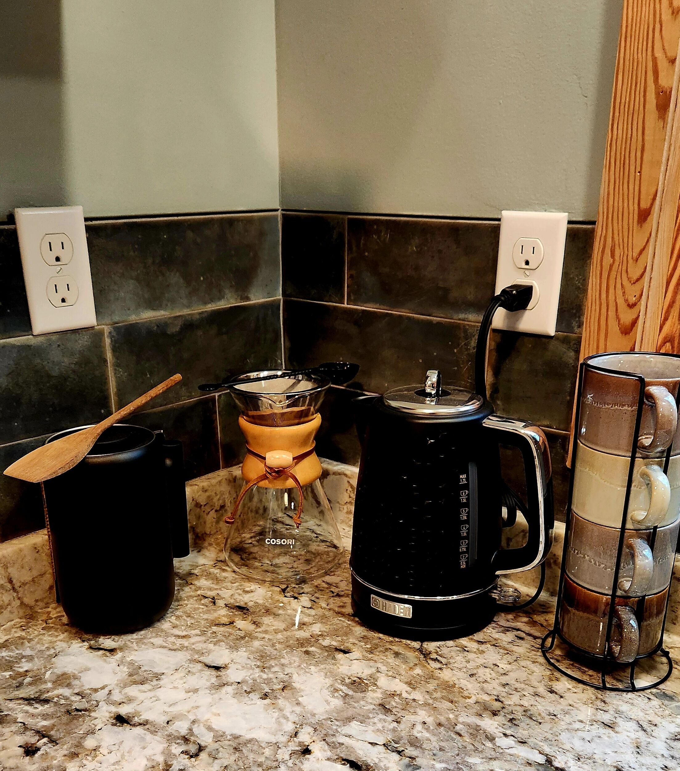 Una cocina con cafetera, hervidor y un recipiente de vidrio sobre la encimera.
