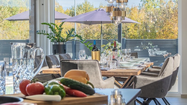 Un espace de restauration en plein air avec une table dressée pour deux personnes, entourée de chaises, et offrant une vue sur les arbres et un ciel dégagé.