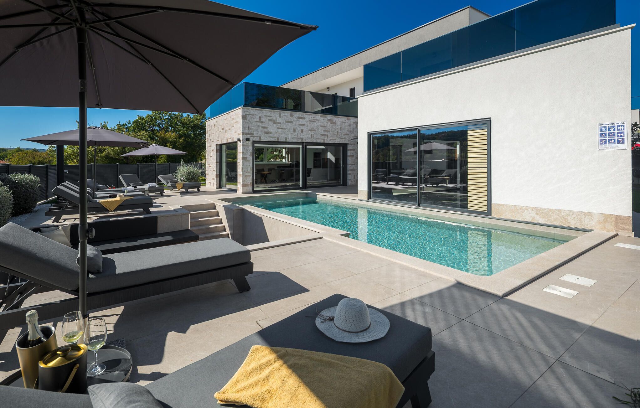 A modern outdoor pool area with lounge chairs, a dining table, and a swimming pool sign.
