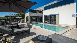 Un espace piscine extérieur moderne, doté de chaises longues, d’une table à manger et d’un panneau indiquant la présence d’une piscine.