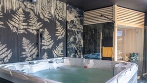 Un espace bien-être comprenant un jacuzzi, un mur en bois orné de motifs de fougères et une douche en verre.