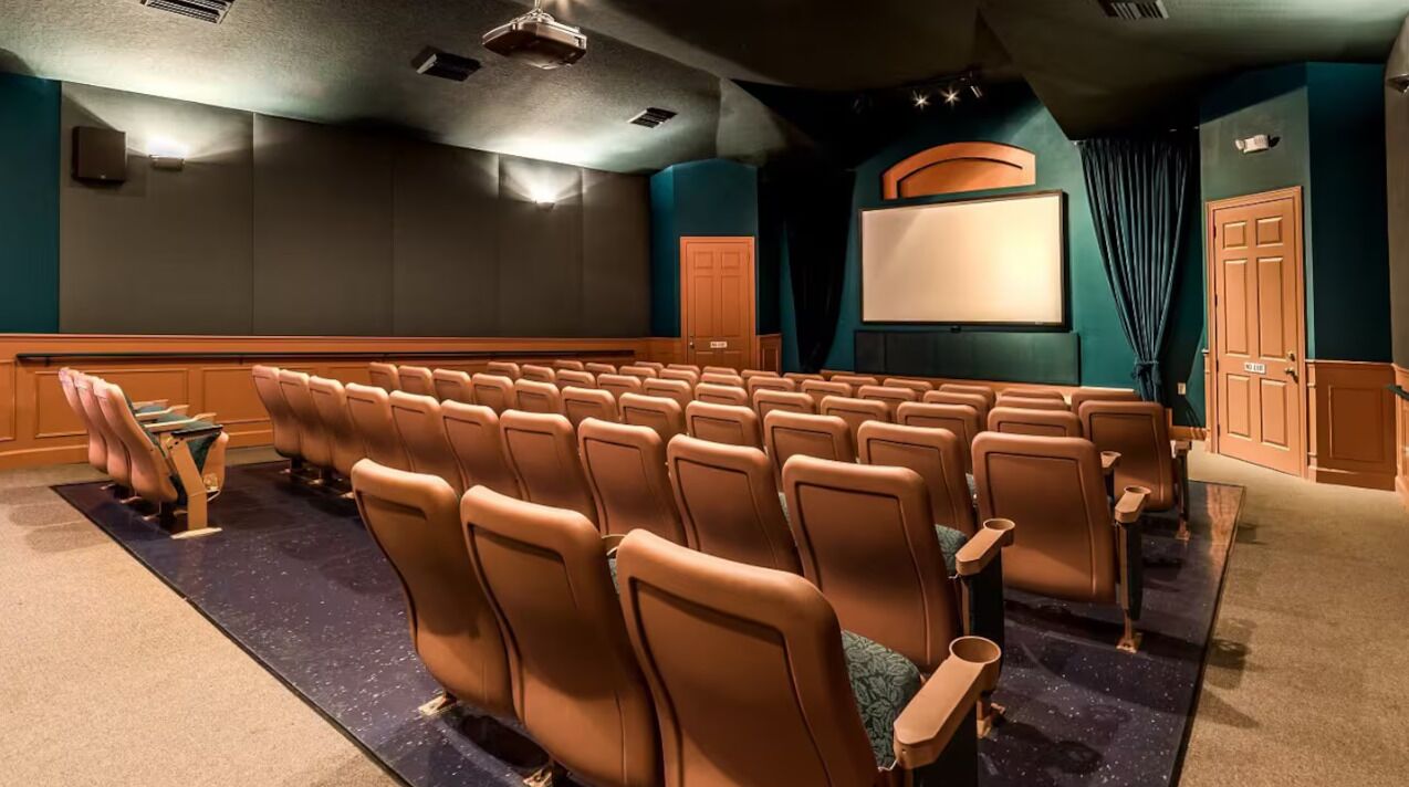 A theater with rows of seats, a screen, and a door.