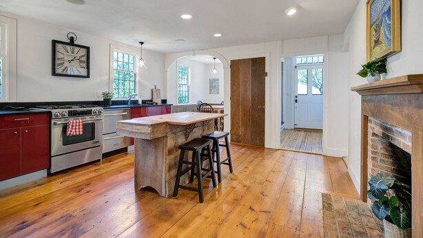 A spacious kitchen with wooden flooring, a central island, and a fireplace.
