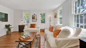 A spacious living room with a white sofa, a wooden coffee table, and a large window with a view of trees.