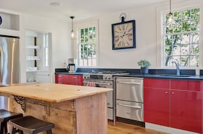 Una cocina con isla de madera, electrodomésticos de acero inoxidable, armarios rojos y un reloj en la pared.