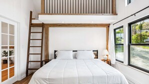 A bedroom with a lofted sleeping area, a ladder, a bedside table with a lamp, and a view of the outdoors through large windows. - The Barn at Winterfound Farm with Hot Tub & Views (Woodstock)