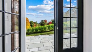 A door leading to a patio with a view of a garden and trees. - The Barn at Winterfound Farm with Hot Tub & Views (Woodstock)