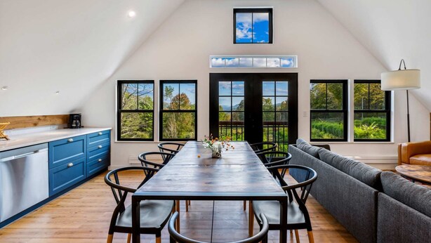 A modern kitchen with a dining area, large windows, and a loft-style ceiling. - The Barn at Winterfound Farm with Hot Tub & Views (Woodstock)