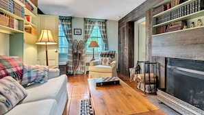 A cozy living room with a fireplace, a sofa, a chair, and a bookshelf filled with books. - Historic Riverside Home with Sauna & Covered Porch (Woodstock)