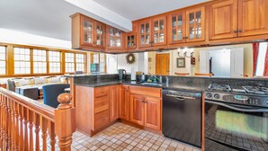 A kitchen with wooden cabinets, a dishwasher, a stove, and a large window. - Historic Riverside Home with Sauna & Covered Porch (Woodstock)