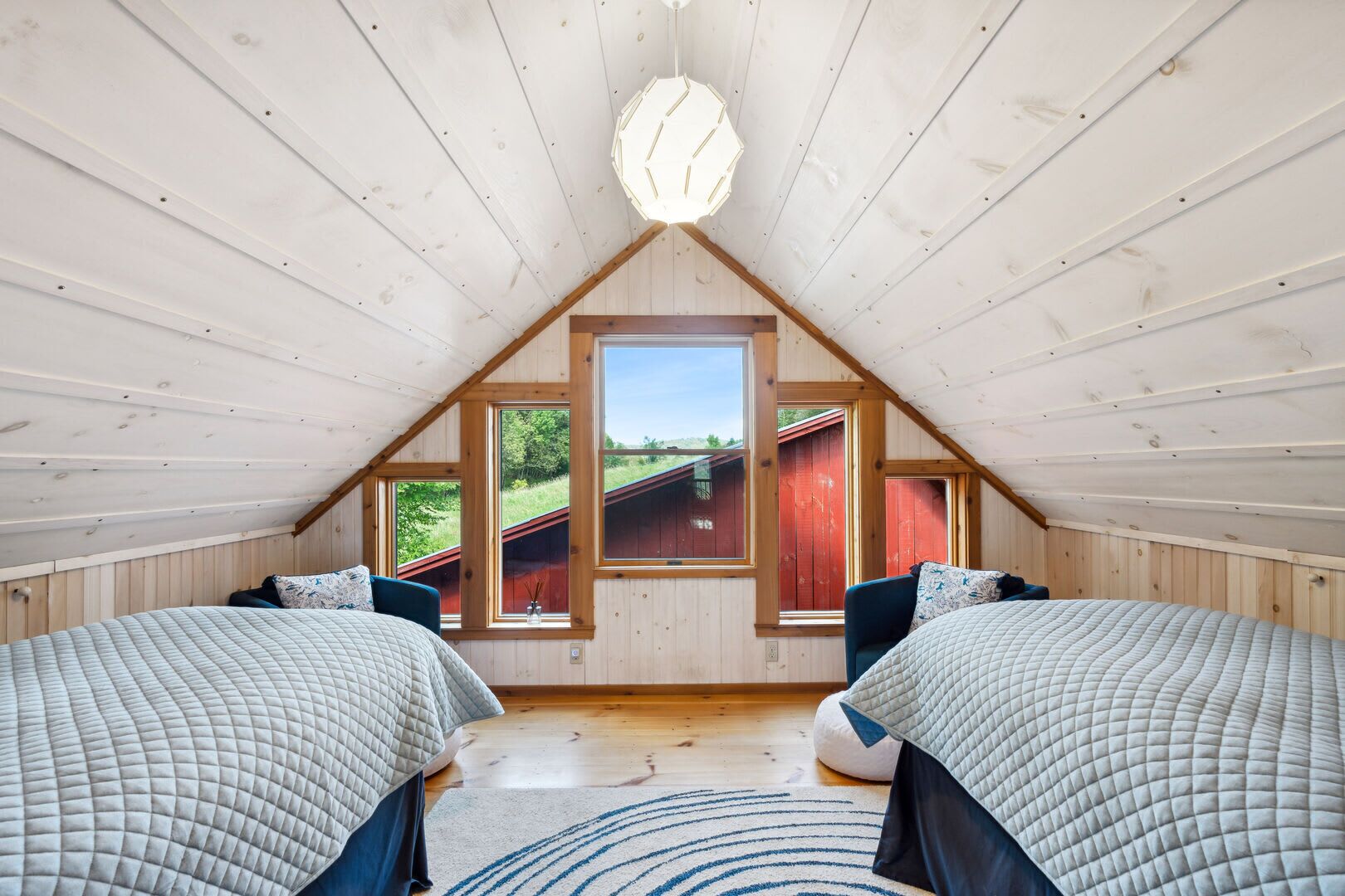 Ein Zimmer mit zwei Betten, Holzwänden, einer geneigten Decke und großen Fenstern.