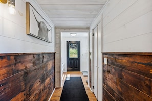 A hallway with wooden paneling, a black door, and a framed picture on the wall.