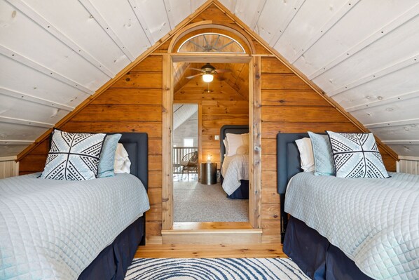 Een slaapkamer met twee bedden, houten wanden, een schuine balkenkap en uitzicht door een deuropening.