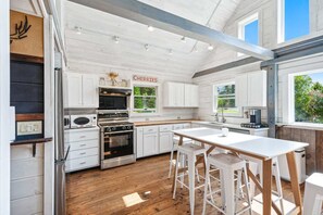 A spacious kitchen with white cabinetry, a central island, and a view of the outdoors. - Scenic Ridge Cabin with Sweeping Vermont Views (Woodstock)