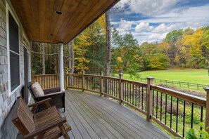 A wooden deck with a view of a golf course and autumn trees.