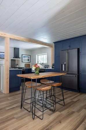 Eine moderne Küche mit dunkelblauen Schränken, einem Edelstahlkühlschrank und einem Holzespeisetisch mit Barhocker.