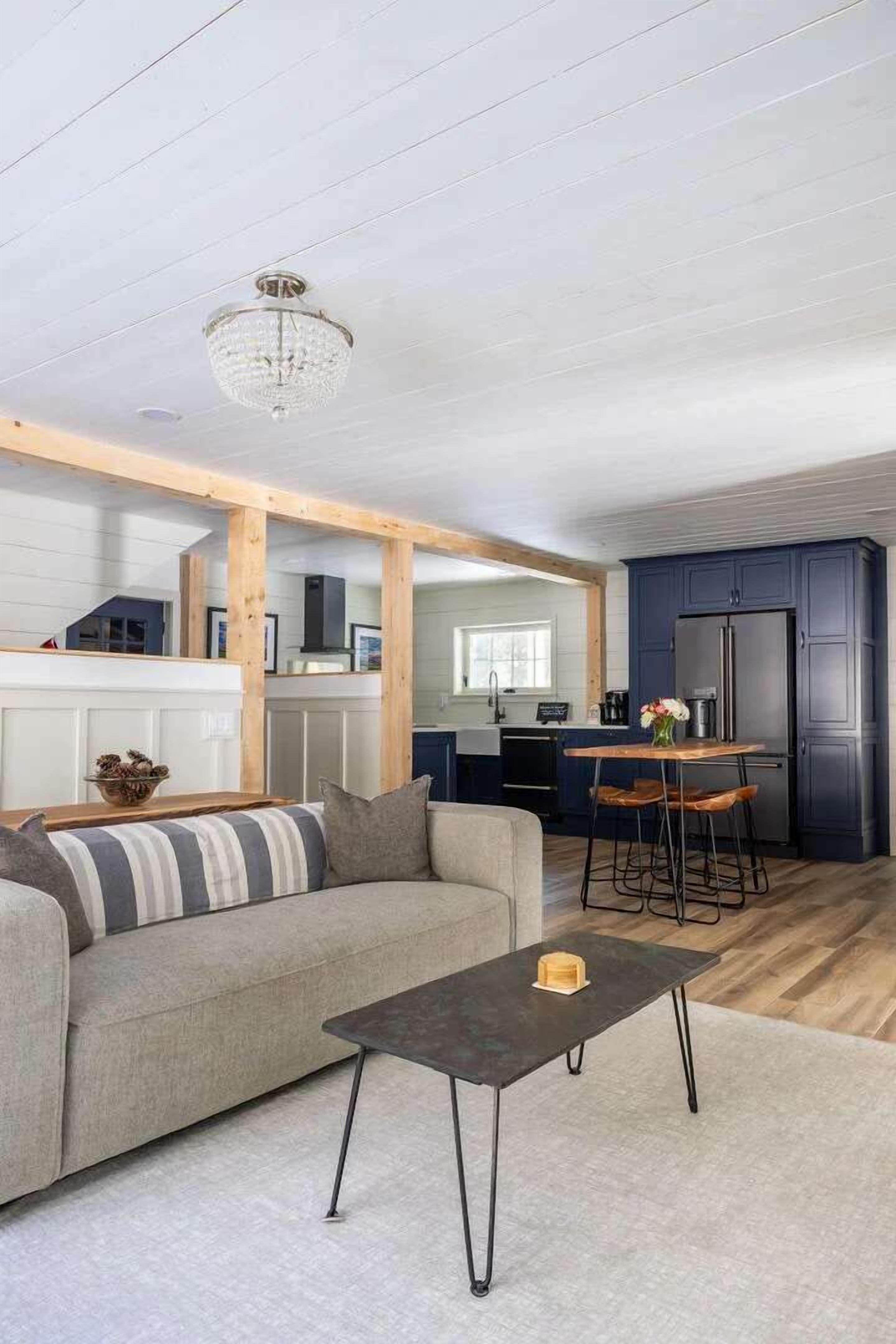 A modern living room with a sofa, a coffee table, and a kitchen area with dark cabinets and a refrigerator.