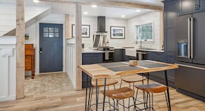 A modern kitchen with a wooden table and stools, a built-in oven, and a refrigerator.