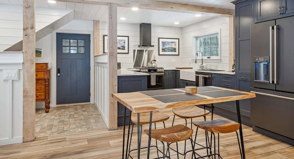 Une cuisine moderne avec une table et des tabourets en bois, un four encastré et un réfrigérateur.
