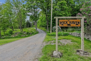 Eine ländliche Straße mit einem hölzernen Schild, auf dem 'Rock Haven' steht und Bären abgebildet sind.