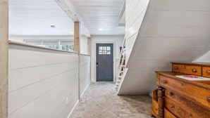 Un couloir étroit avec une commode en bois, une porte et un escalier.