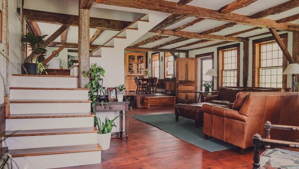 Ein rustikales Interieur mit sichtbaren Holzbalken, einer Treppe, einem Essbereich und Ledermöbeln.