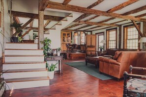 A rustic interior with exposed wooden beams, a staircase, a dining area, and leather furniture. - Historic Farmhouse on Working VT Farm & Hot Tub (Woodstock)
