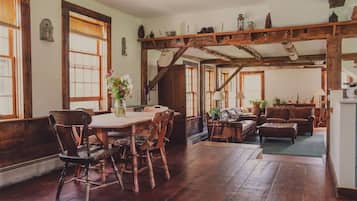 A rustic interior with a wooden dining table, chairs, a sofa, and a staircase.