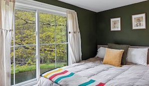 Un dormitorio con un ventanal grande, una cama con un edredón colorido y dos cuadros en la pared.