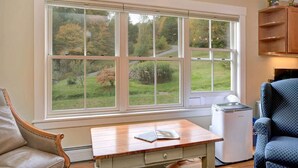 A room with a large window, a wooden table, a chair, and a small white appliance.
