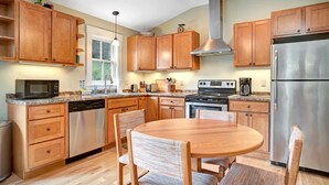 A kitchen with wooden cabinets, stainless steel appliances, a dining table with chairs, and a window.