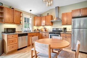Una cocina con armarios de madera, electrodomésticos de acero inoxidable, una mesa de comedor con sillas y una ventana.