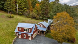 A two-story house with a blue roof, a stone foundation, and a driveway leading to the garage.