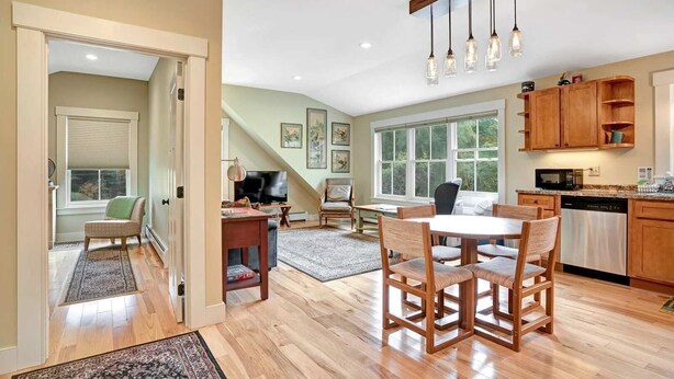 A spacious living area with a dining table, kitchen, and large windows.