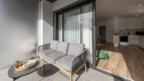 Una sala moderna con un sofá gris, una mesita con una bandeja de objetos y un suelo de vidrio corredero que da a una zona de cocina.