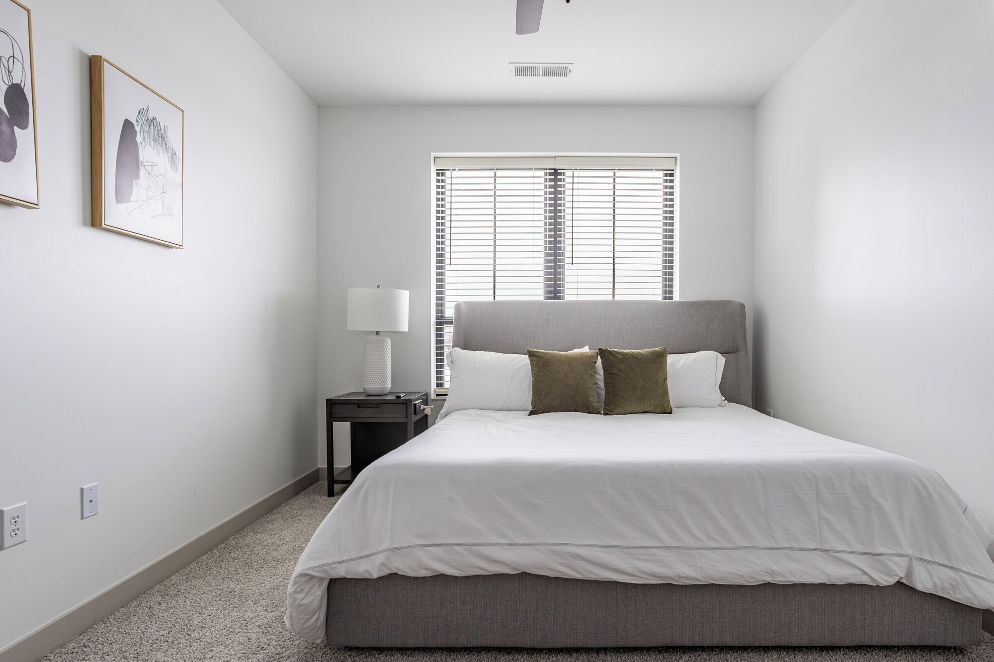 Un dormitorio con cama, mesita de noche, lámpara y ventana con persianas.