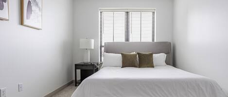 Un dormitorio con cama, mesita de noche, lámpara y ventana con persianas.