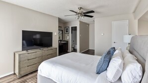 A bedroom with a bed, a TV, a ceiling fan, a dresser, and a bathroom visible through an open door. - Landing Grand Prairie (Grand Prairie)