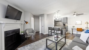 A modern living room with a fireplace, a television, a dining area, and a kitchen. - Landing Grand Prairie (Grand Prairie)