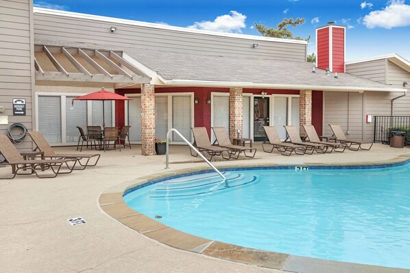 A pool area with lounge chairs and a red umbrella. - Landing Grand Prairie (Grand Prairie)