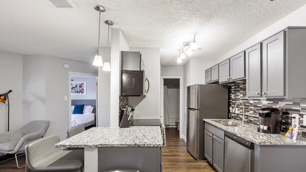 A modern kitchen with granite countertops, stainless steel appliances, and a central island with bar stools. - Landing Grand Prairie (Grand Prairie)
