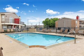 A swimming pool with lounge chairs and a lifeguard tower, surrounded by buildings and a clear sky. - Landing Grand Prairie (Grand Prairie)