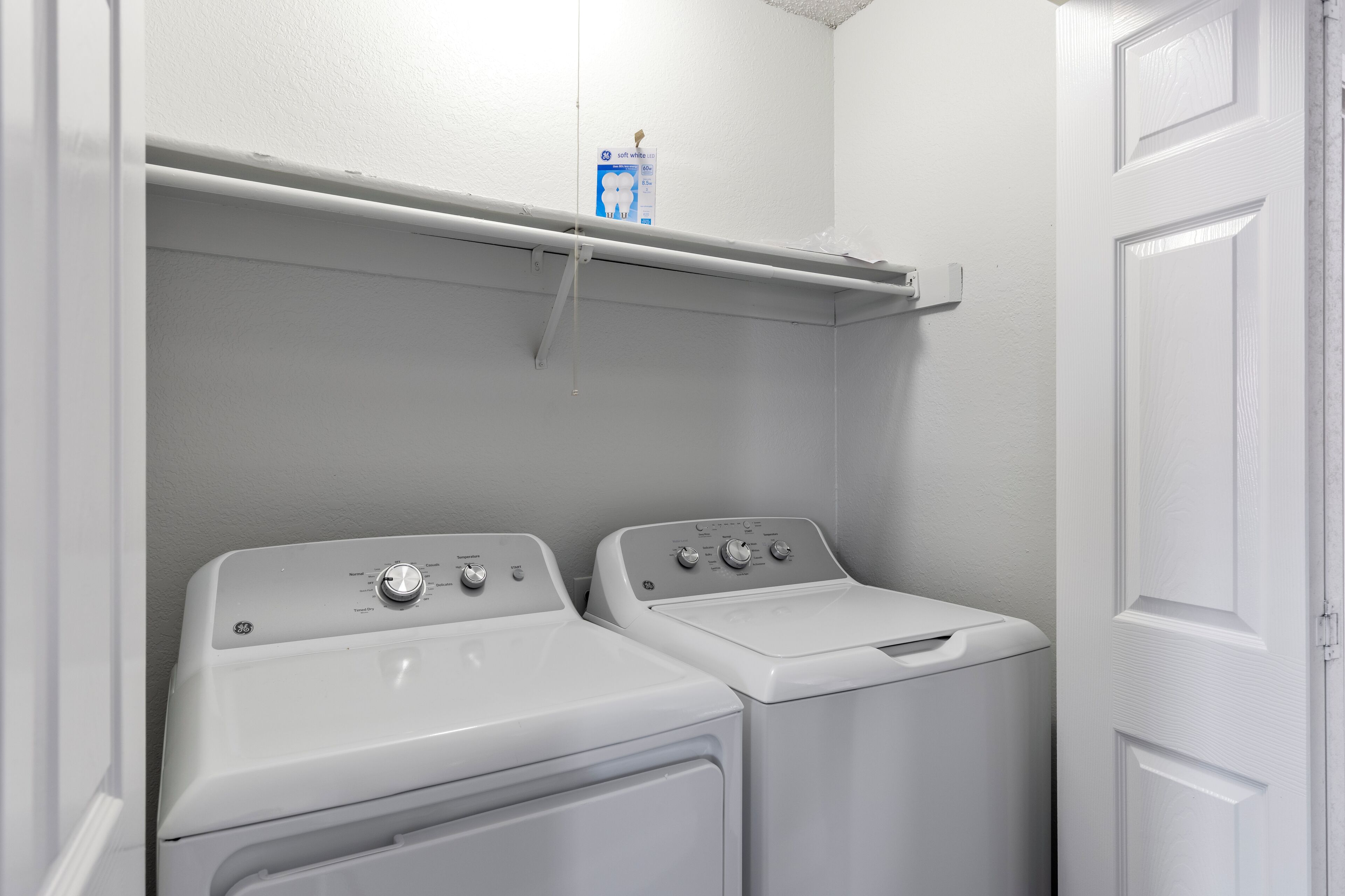 A laundry area with two white front-loading washing machines and a shelf above them.